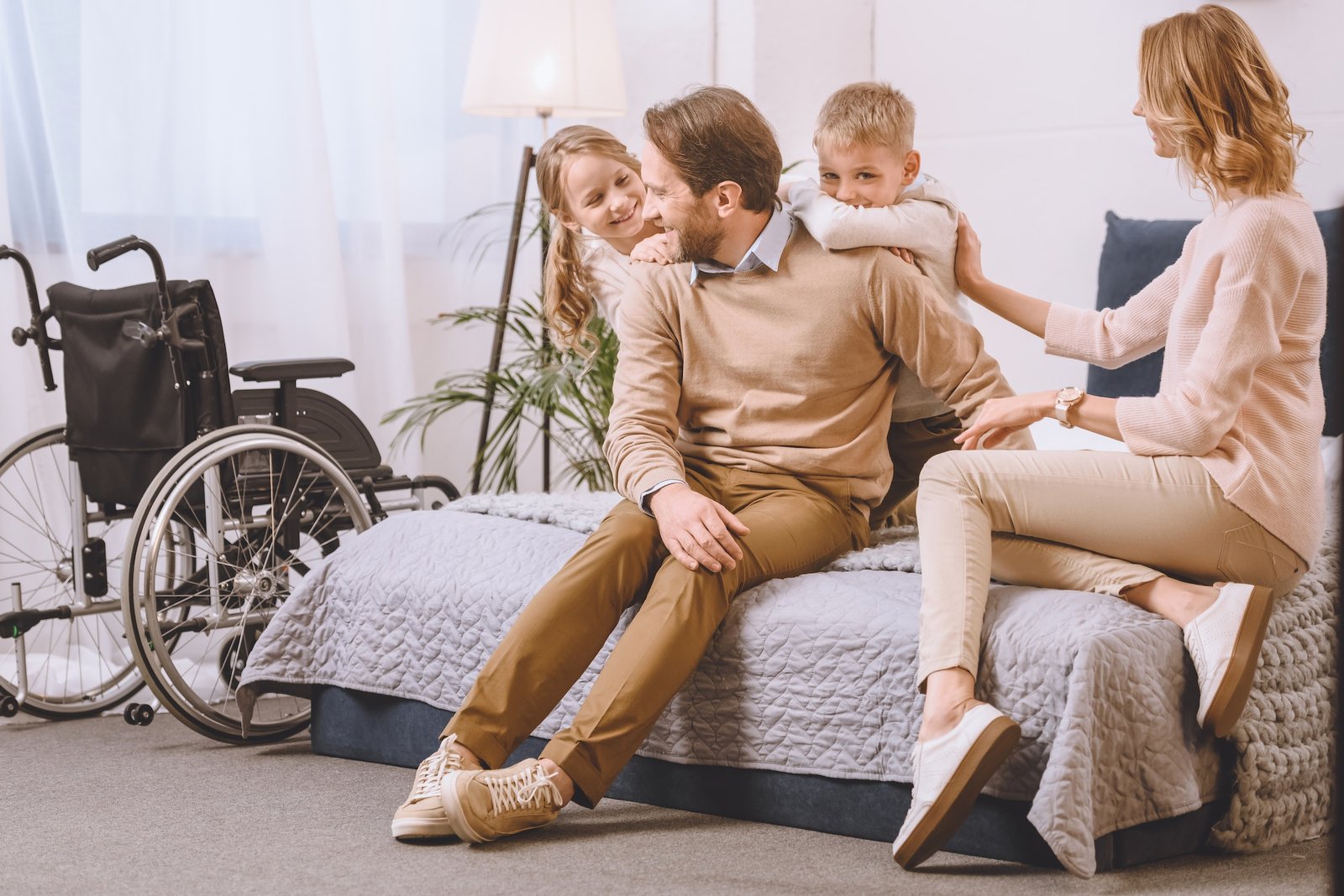 happy father with disability and mother sitting with kids on bed